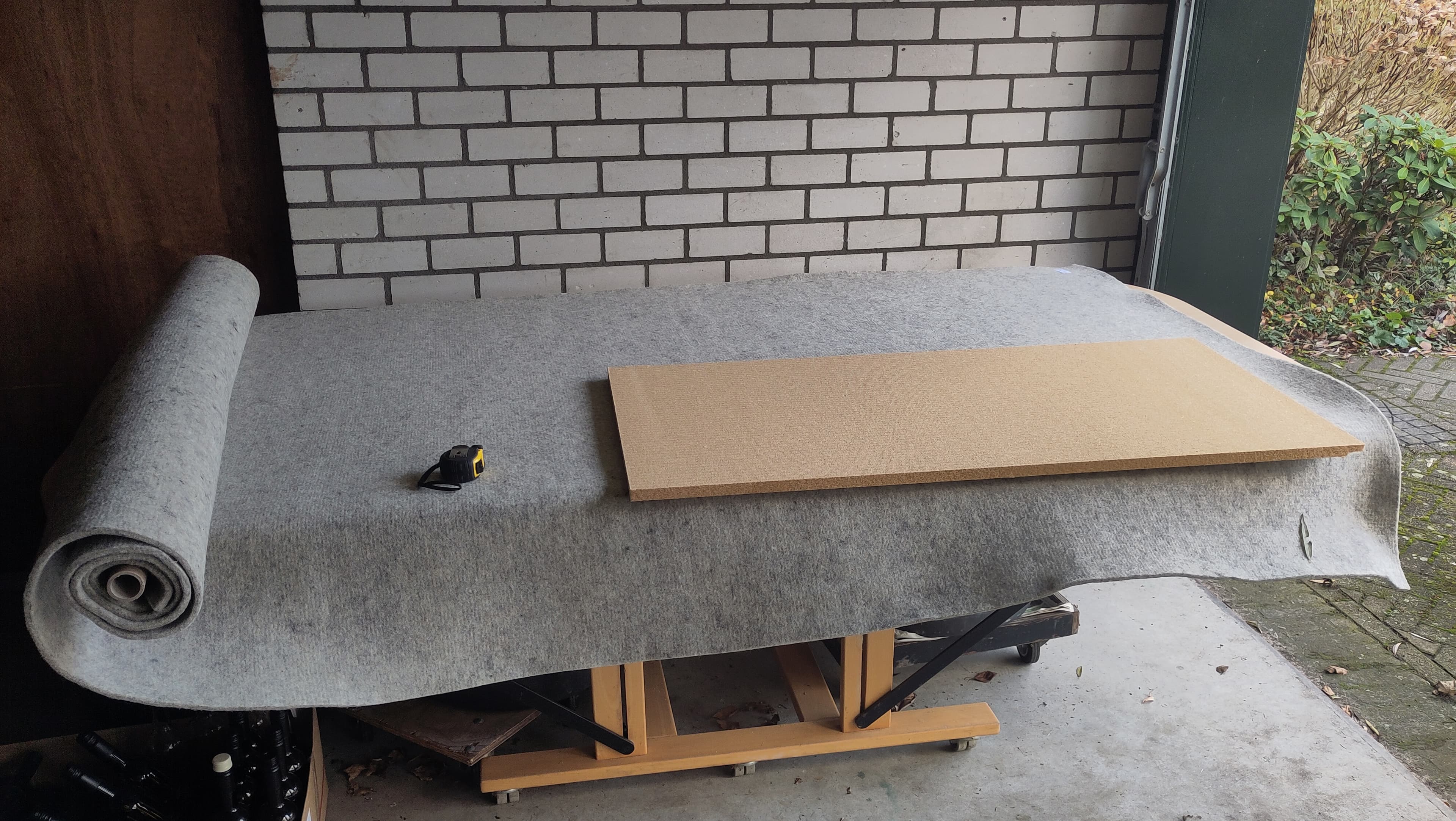 Grijs vilt op een werkbank met een houten plaat en rolmaat voor een bakstenen muur.